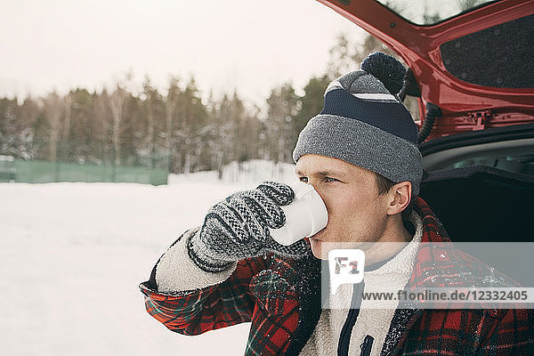 Man drinking coffee in car trunk at park during winter