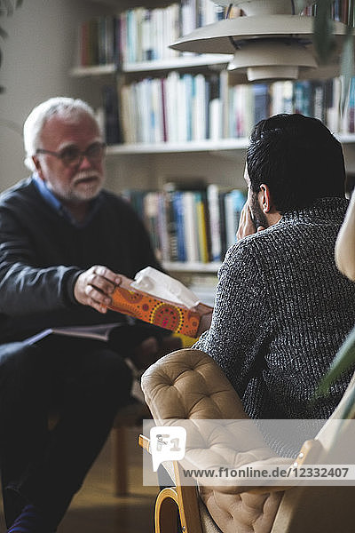 Therapist giving tissue box to male patient at home office