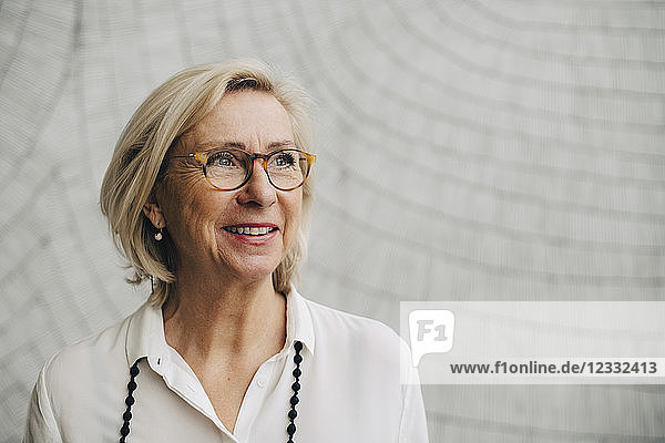 Thoughtful smiling senior businesswoman against wall in office