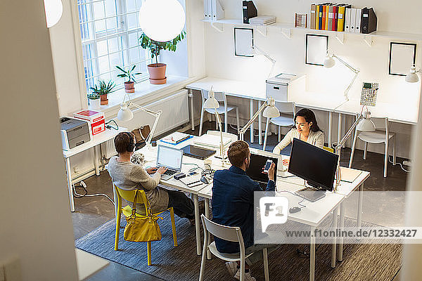 High angle view of multi-ethnic colleagues using technologies at desk in creative office