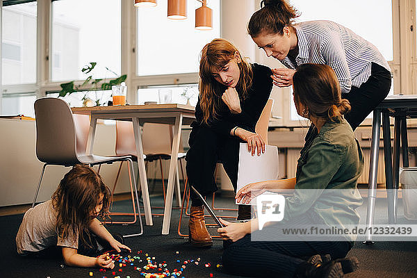 Female colleagues discussing over laptop by boy playing on floor at creative office
