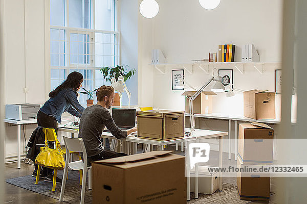 Business colleagues working at desk amidst cardboard boxes in illuminated creative office