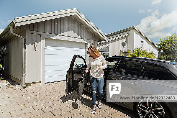 Full length of woman standing by car outside house on sunny day