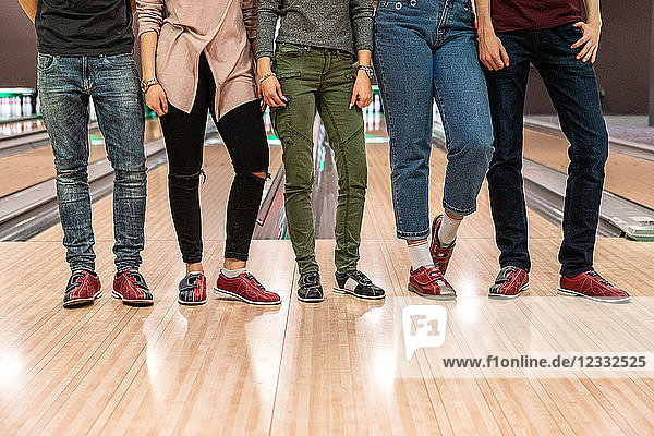 Low section of multi-ethnic friends standing on parquet floor at bowling alley