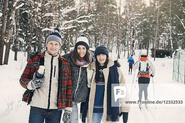 Portrait of smiling friends standing on snow covered field at park