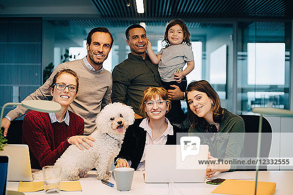 Portrait of smiling business team with kid and dog at creative office