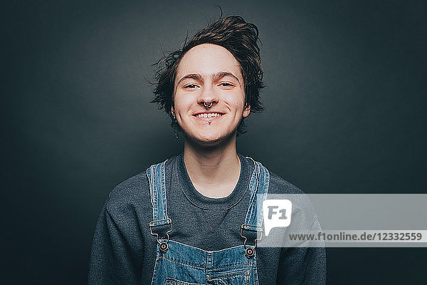 Portrait of smiling young man wearing denim overalls over gray background