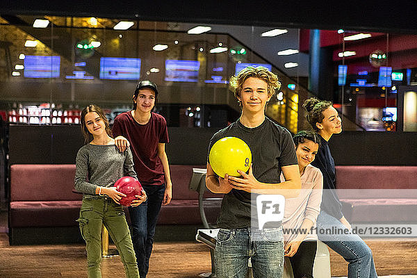 Portrait of smiling teenage boy holding ball while standing against friends at bowling alley