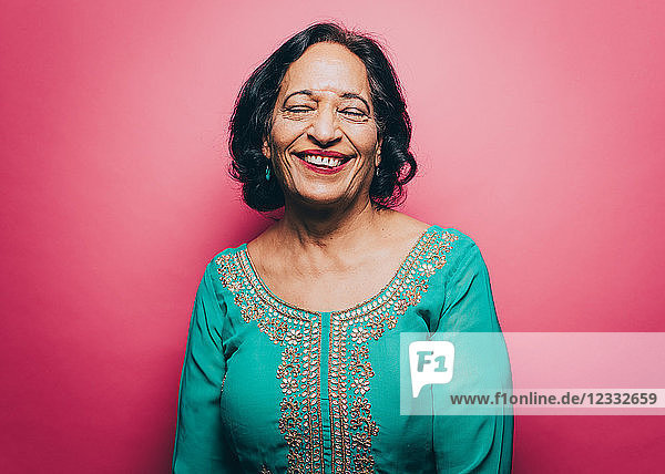 Smiling senior woman with eyes closed over pink background