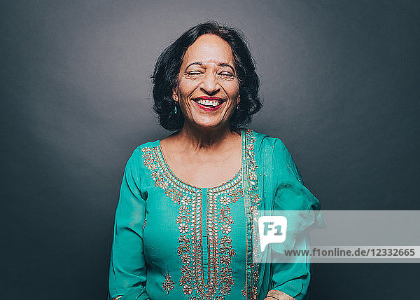 Smiling senior woman with eyes closed standing against gray background