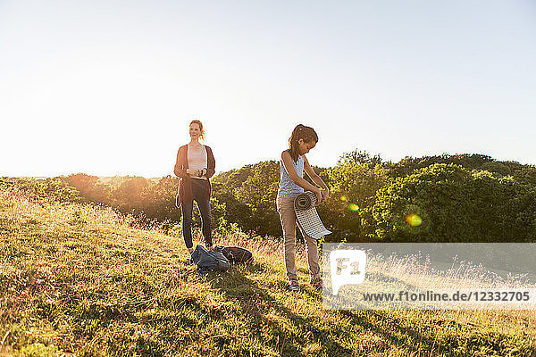Full length of girl rolling mat while standing by mother on field against sky during sunset