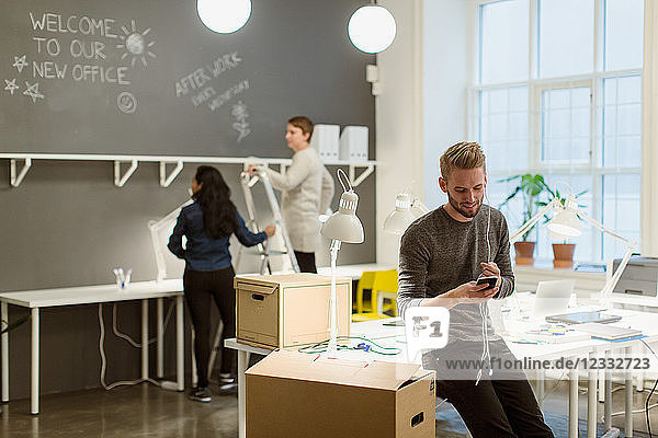 Young businessman talking on smart phone while female colleagues working by wall at creative office