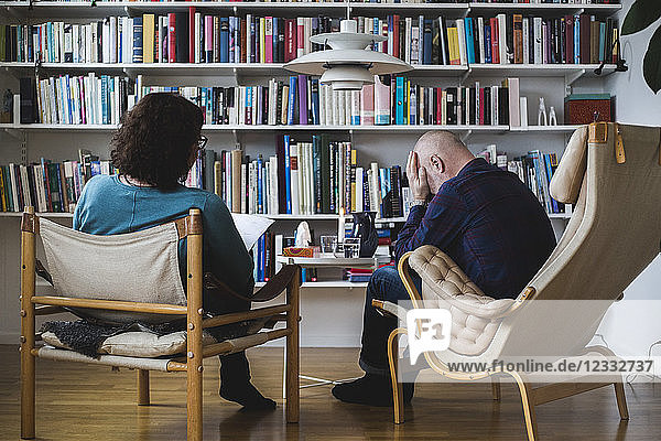 Depressed patient and female therapist in front of bookshelf at home office