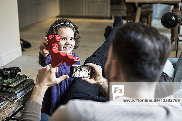 Smiling daughter showing red block to fathers resting in living room