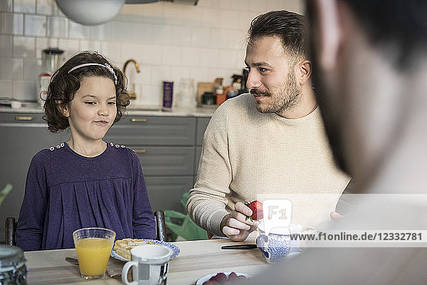 Father looking at daughter while having breakfast in kitchen