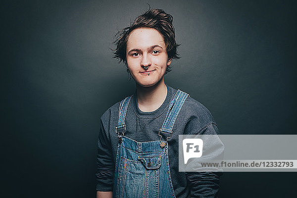 Portrait of smiling young man wearing denim overalls over gray background