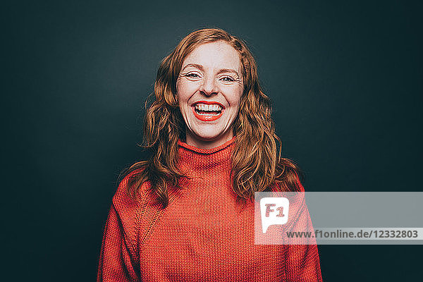 Portrait of woman in orange top laughing against gray background