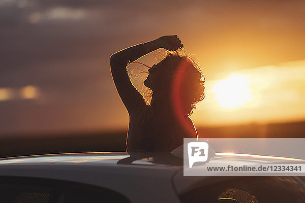 Woman outside the car at sunset raised arm
