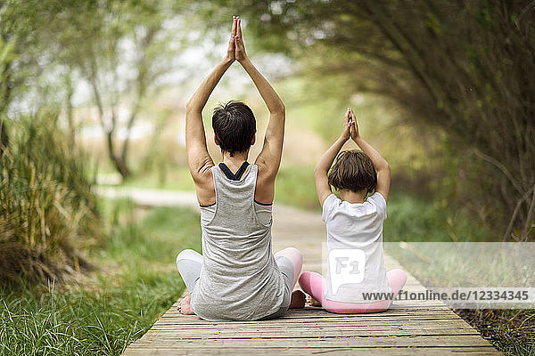 Rear view of mother and daughter doing yoga on boardwalk