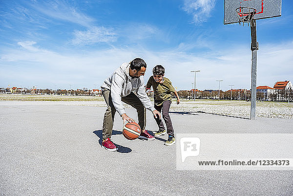 Father and son playing basketball on court outdoors