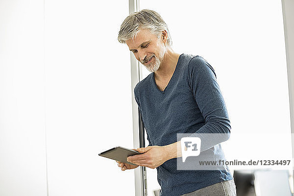 Mature man standing in his office  using digital tablet