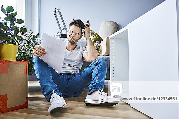 Frustrated man reading instructions while assembling furniture in new apartment