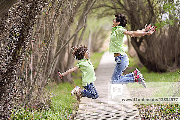 Happy mother and daughter jumping on boardwalk