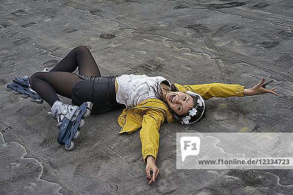 Screaming young woman with inline skates lying on ground listening music with headphones