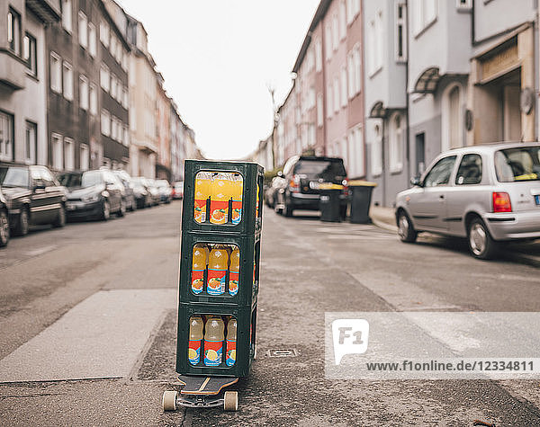Stack of three boxes with lemonade bottles standing on longboard on the street