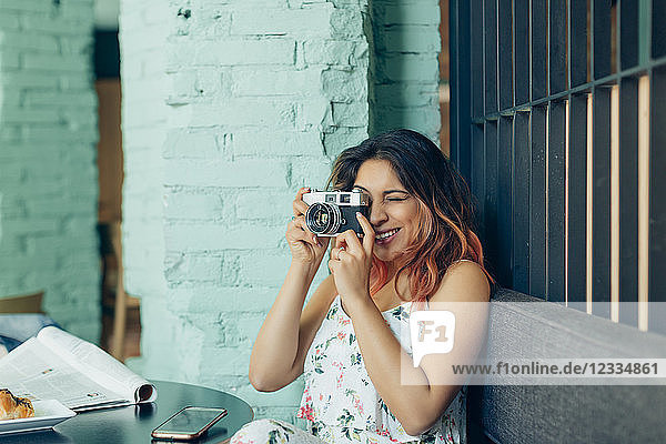 Smiling woman sitting in coffee shop taking pictures with camera