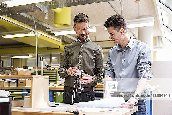 Two smiling men with plan looking at product in factory