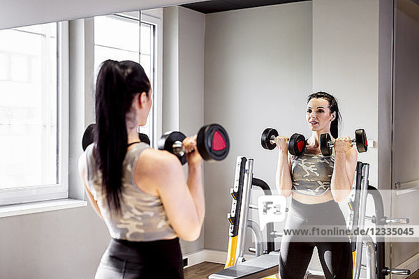 Woman lifting dumbbells in gym looking in mirror