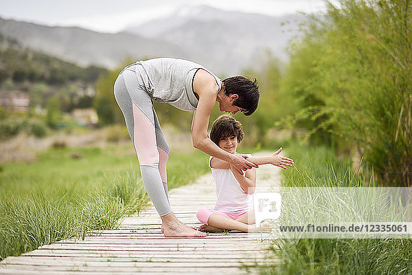 Mother explaining yoga position to daughter on boardwalk