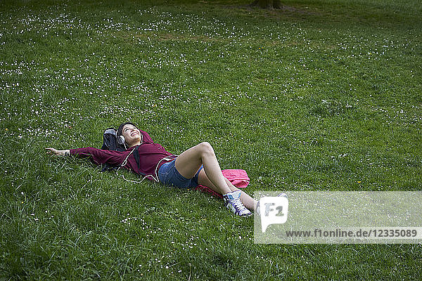 Young woman lying on a meadow listening music with headphones and cell phone
