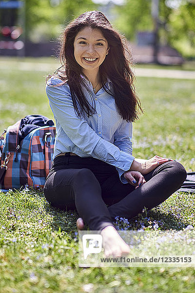 Portrait of smiling young woman sitting barefoot on a meadow