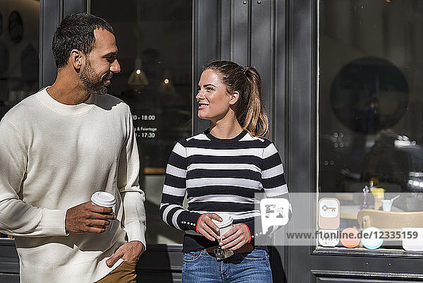 Man and woman holding takeaway cups outside a cafe talking