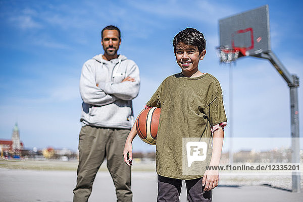 Portrait of boy with father on basketball court outdoors
