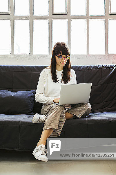 Young woman sitting on couch in office using laptop
