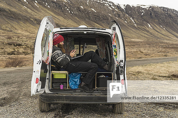 Iceland  man sitting in van using smartphone and laptop