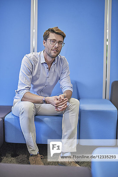 Portrait of businessman sitting on light blue stool in an office