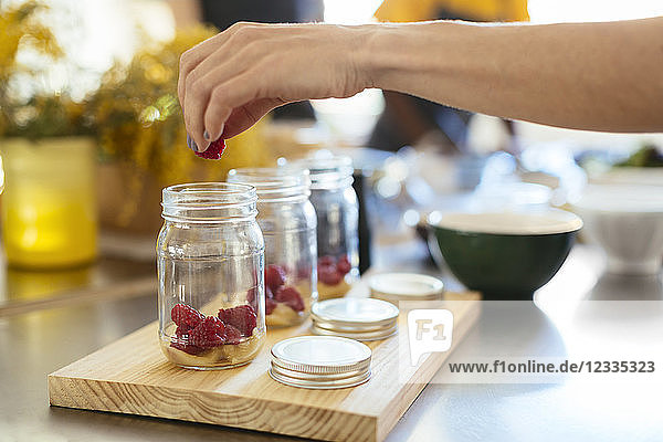 Close-up of woman in kitchen putting raspberry into jar