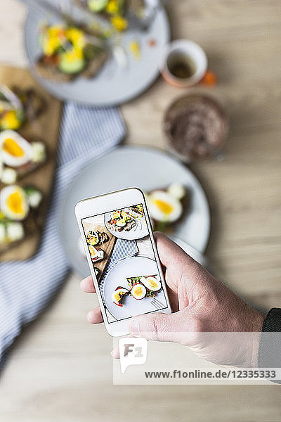 Man holding smartphone with photo of vegetarian breakfast with bread and eggs