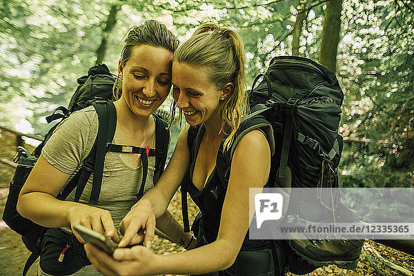 Two happy young women on a hiking trip using cell phone