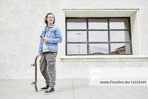 Young man holding skateboard  using smartphone