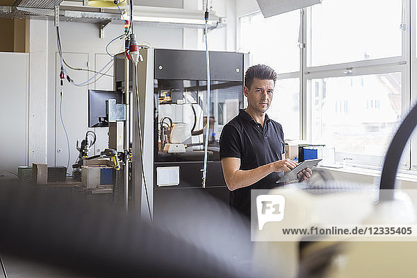 Man standing in factory with tablet looking at machine