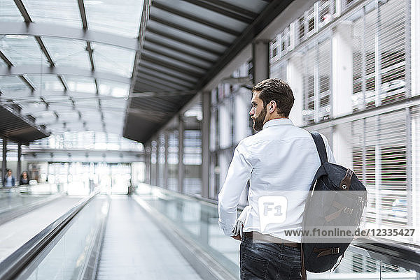 Young businessman with backpack on moving walkway