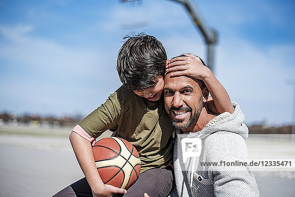 Portrait of happy father and son with basketball outdoors