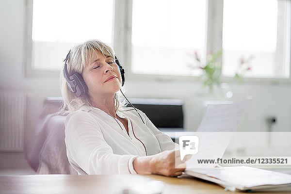 Relaxed mature businesswoman wearing headphones at desk