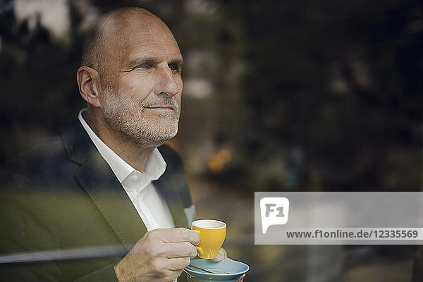 Senior businessman standing by window  drinking coffee