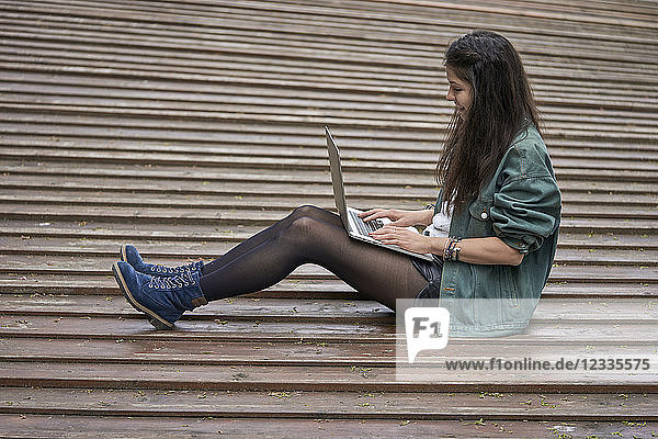 Young woman sitting on ground outdoors using laptop